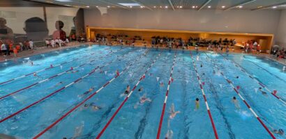 Ein Foto, das aus der Vogelperspektive das große Schwimmbecken beim Neujahrsschwimmfest zeigt, zahlreiche Schwimmer sind im Wasser und bereiten sich auf den Wettkampf vor.