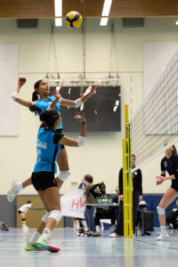 Ein Foto von einer VTH-Spielerin, die direkt am Netz hochspringt und dabei mit dem Arm ausholt, um den Ball über das Netz zu schlagen.