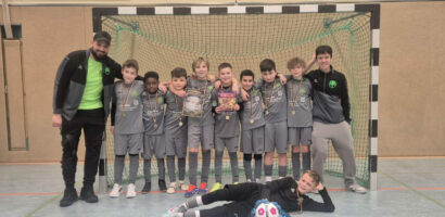 Ein Gruppenfoto der HNT-Mannschaft am Sonntag, auf dem die Spieler in einer Reihe nebeneinander vor einem Tor stehen und Medaillen um den Hals haben.