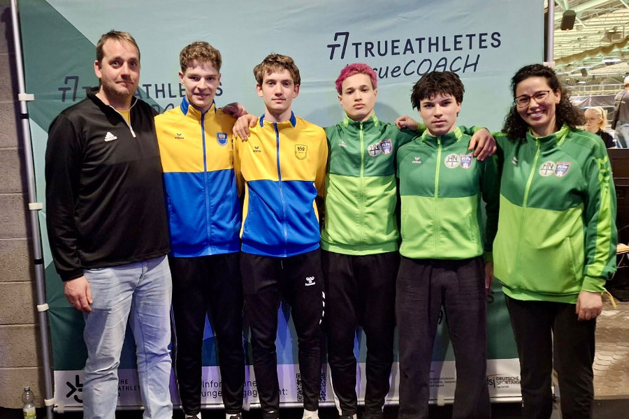 Ein Foto der Staffel HNT-BSV, auf dem die vier Athleten dicht nebeneinander stehen, die Arme jeweils auf die Schultern des Nebenmannes gelegt; eingerahmt werden sie von ihren Trainern.