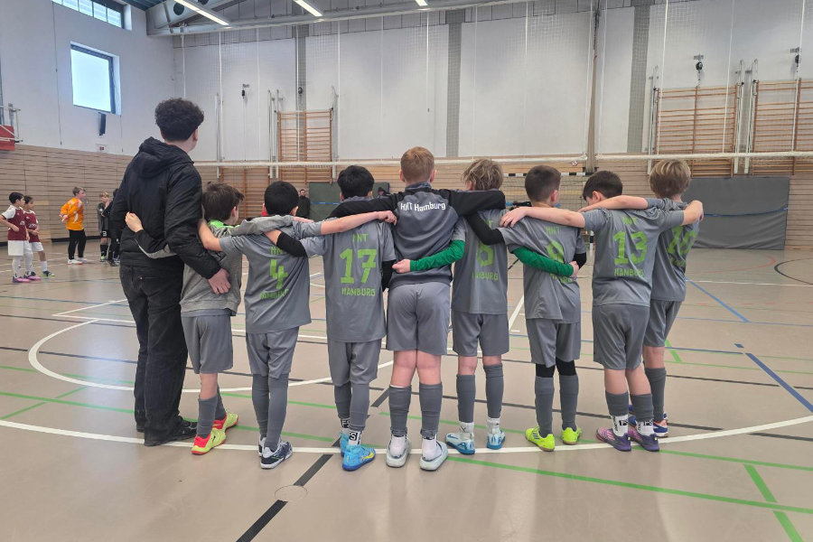 Ein Foto von der 1. E-Jugend der HNT, auf dem die Spieler mit dem Rücken zur Kamera nebeneinander stehen und die Arme um die Schultern des Nebenmannes gelegt haben.