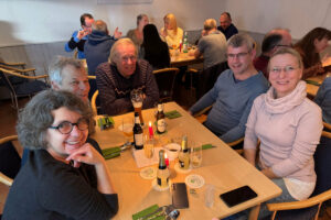 Ein Foto von Gästen, die beim Happy-Hours-Event "Menu retour" an einem der Tische sitzen; alle schauen zur Kamera und lächeln freundlich.