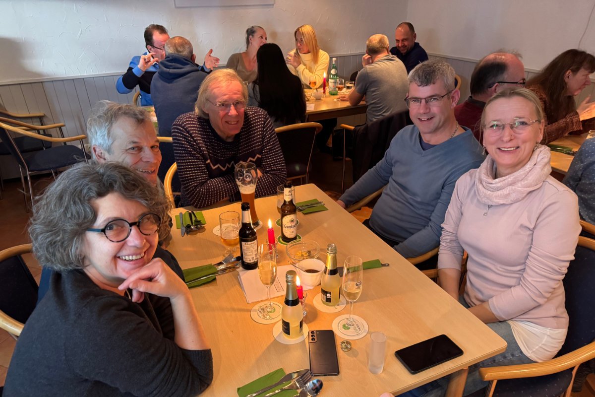 Ein Foto von Gästen, die beim Happy-Hours-Event "Menu retour" an einem der Tische sitzen; alle schauen zur Kamera und lächeln freundlich.