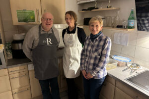 Ein Foto von drei Personen, die beim Happy-Hours-Event "Menu retour" in der Küche stehen und freundlich in die Kamera lächeln.