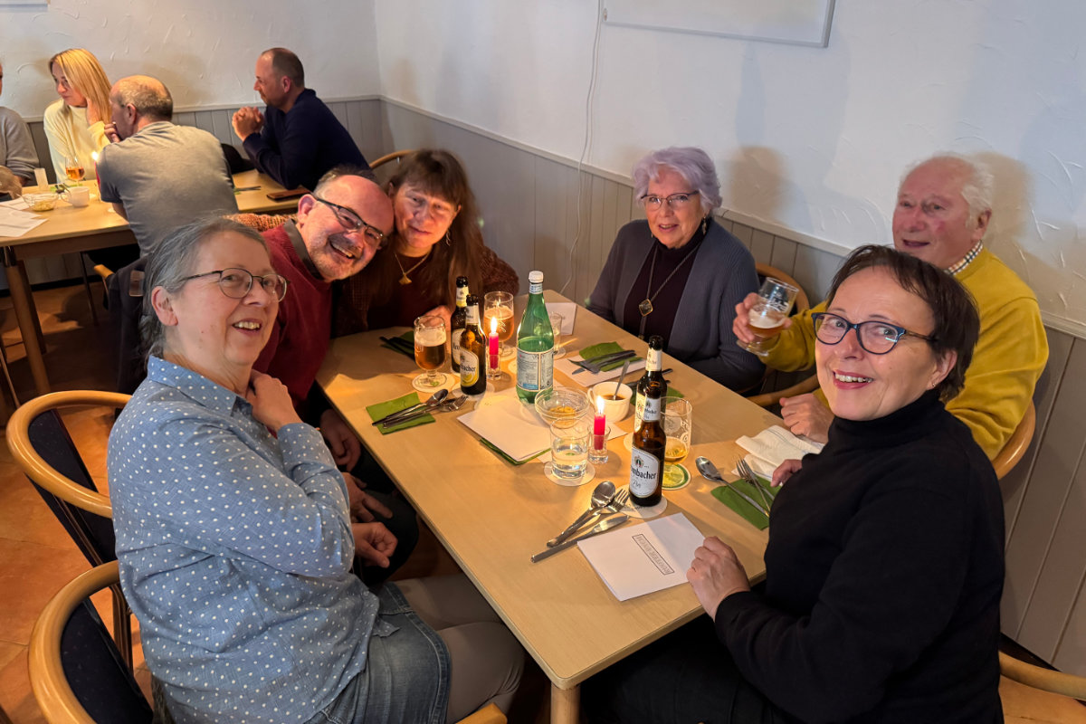 Ein Foto von Gästen, die beim Happy-Hours-Event "Menu retour" an einem der Tische sitzen; alle schauen zur Kamera und lächeln freundlich.