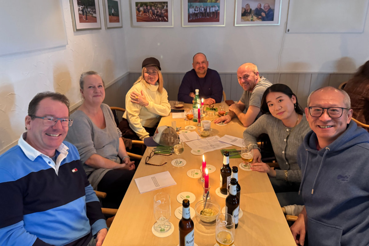 Ein Foto von Gästen, die beim Happy-Hours-Event "Menu retour" an einem der Tische sitzen; alle schauen zur Kamera und lächeln freundlich.