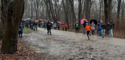 Ein Foto von der schlammigen Laufstrecke beim "Swim & Run" im Volkspark, zwei Teilnehmer laufen mit dem Rücken zur Kamera und am Rand stehen zahlreiche Zuschauer mit Regenschirmen.