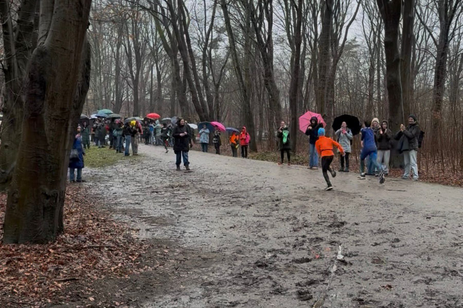 Ein Foto von der schlammigen Laufstrecke beim "Swim & Run" im Volkspark, zwei Teilnehmer laufen mit dem Rücken zur Kamera und am Rand stehen zahlreiche Zuschauer mit Regenschirmen.