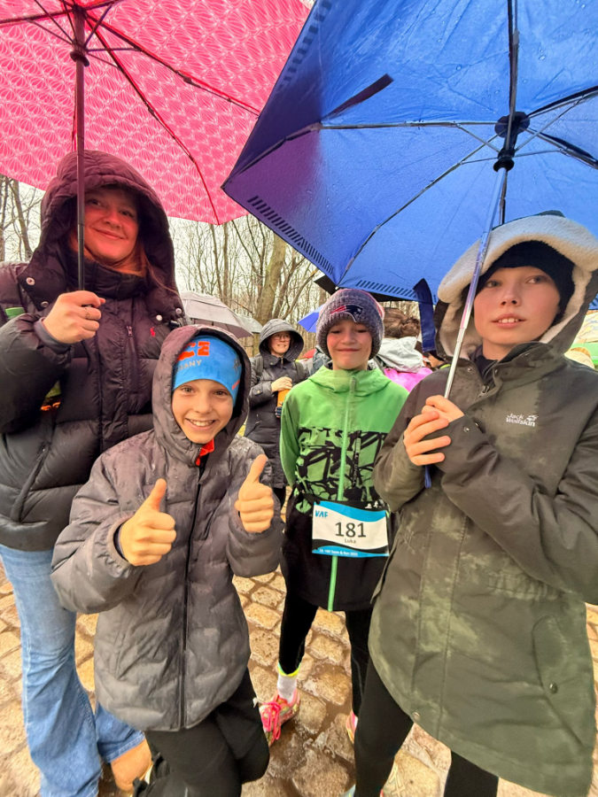 Ein Foto von HNT-Triathleten, die unter Regenschirmen auf den Start warten, einer von ihnen zeigt mit beiden Händen "Daumen hoch" in die Kamera.