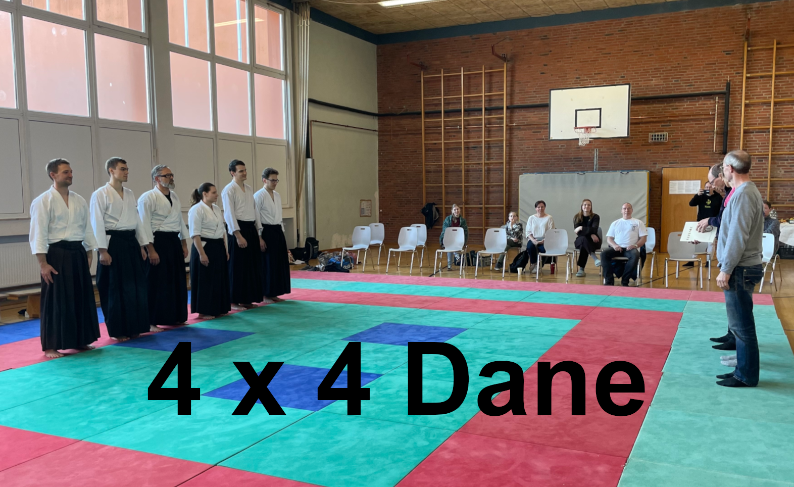 Ein Foto der Prüflinge, die in einer Reihe nebeneinander auf der Matte stehen und auf den Beginn der Prüfung warten.