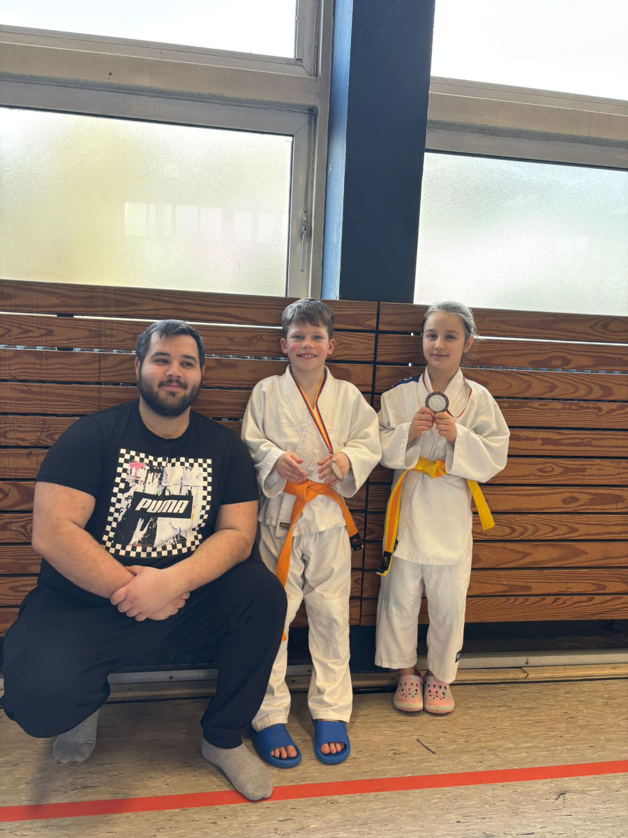 Ein Foto von Mark und Viktoria, die neben ihrem Trainer Max stehen und ihre Bronzemedaillen präsentieren.