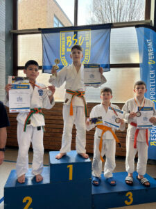 Ein Foto von Mark bei der Siegerehrung, er steht auf der unteren Stufe des Podestes und hält seine Urkunden und seine Bronzemedaille nach oben.