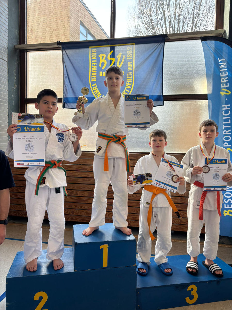 Ein Foto von Mark bei der Siegerehrung, er steht auf der unteren Stufe des Podestes und hält seine Urkunden und seine Bronzemedaille nach oben.