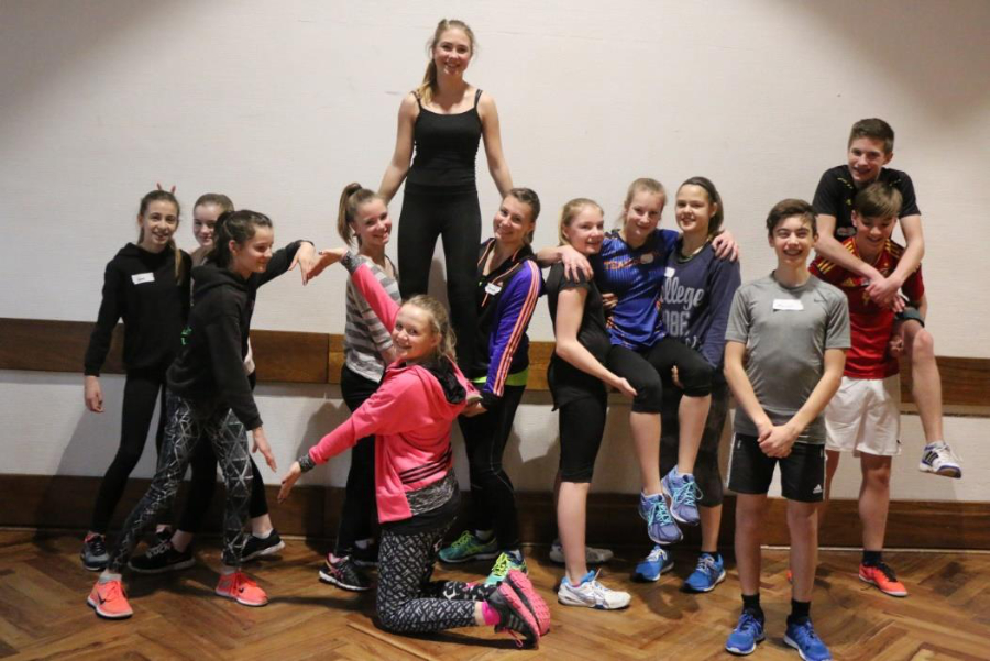 Ein Foto von 13 Jugendlichen, die am HNT Startpiloten teilnehmen und in einer Turnhalle für das Foto posieren, indem sie verschiedene sportliche Übungen zeigen.