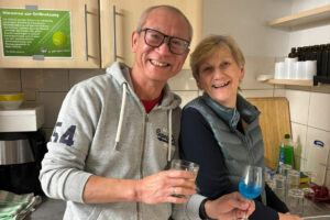 Ein Foto von zwei Gästen, die beim Happy-Hours-Event "Cocktails meet soundtracks" mit ihren Gläsern in der Küche stehen.