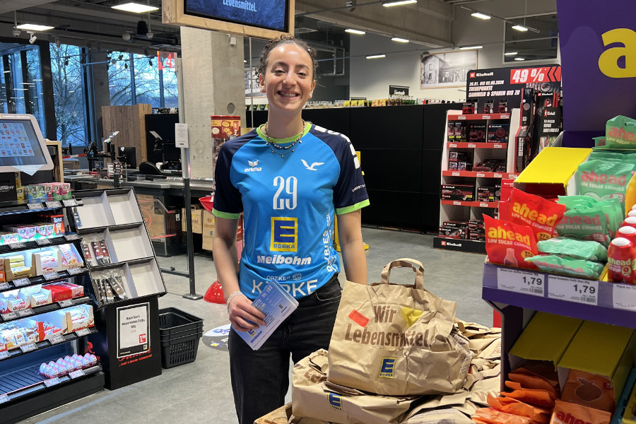 Ein Foto von VTH-Spielerin Sarah Santos Goncalves im Edeka-Markt, neben ihr die vorgepackten Lebensmitteltüten, die gespendet werden konnten.