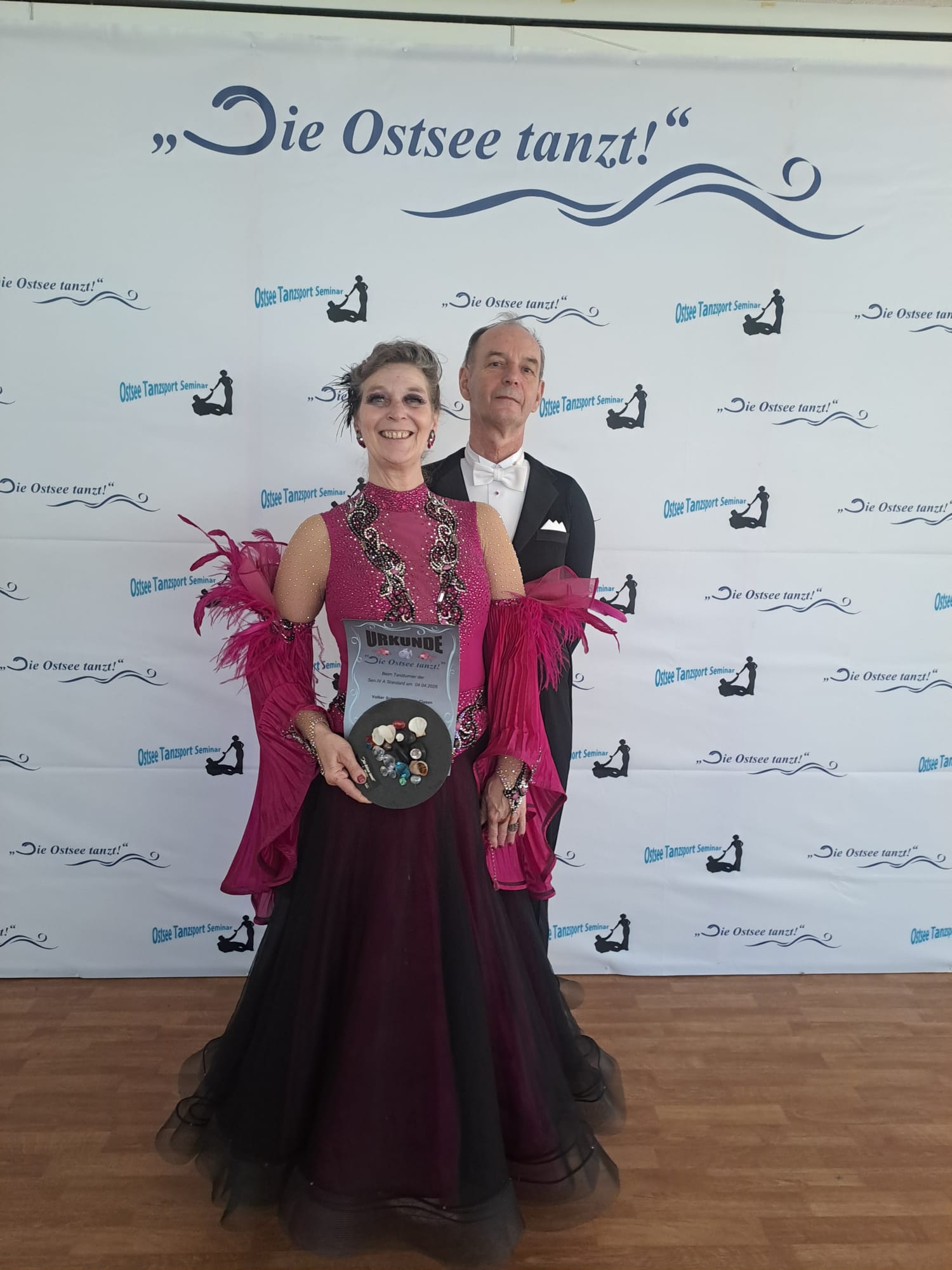 Ein Foto von Caro und Volker bei der Veranstaltung "Die Ostsee tanzt", auf dem die beiden nebeneinander vor einer Fotowand für die Kamera posieren.