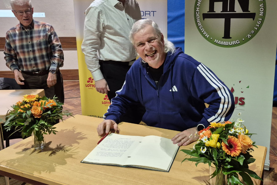 Ein Foto von Michael Richter, auf dem er an einem Tisch vor dem "Grünen Buch" der HNT sitz und in die Kamera lächelt.