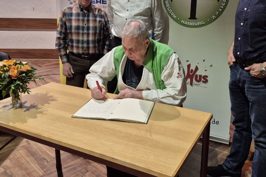 Ein Foto von Hans Kautz, auf dem er am Tisch sitzend in das "Grüne Buch" der HNT schreibt.