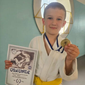 Ein Foto von Matwej, der mit einem Lächeln seine Goldmedaille und seine Urkunde in die Kamera hält.