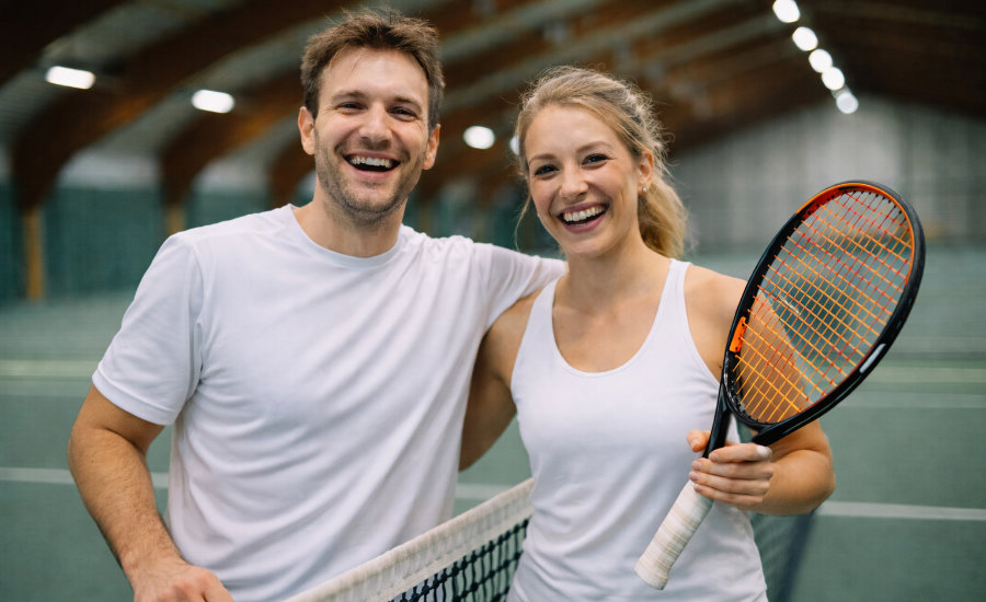 Ein mit KI erstelltes Foto von einem Tennisspieler und einer Tennisspielerin, die gemeinsam am Netz stehen, sich umarmen und freundlich lächeln.