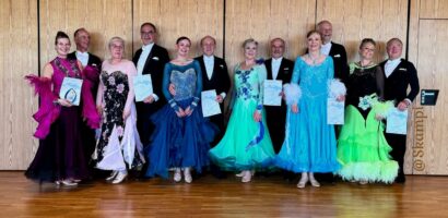 Ein Foto von Caro und Volker, die neben anderen Tanzpaaren stehen und ihre Trophäe und Urkunde präsentieren.