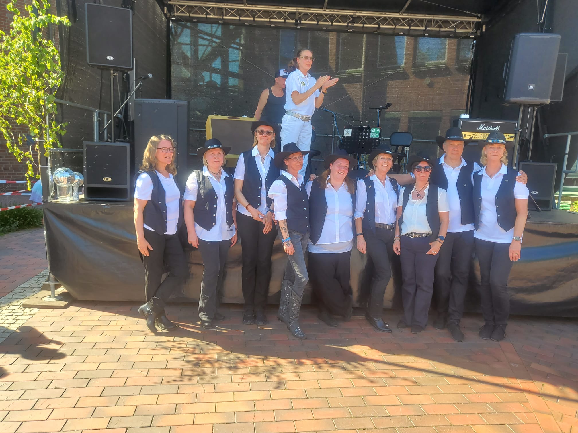 Ein Foto der Auftrittsgruppe der HNT Line Dancer, die auf dem Rathausplatz in Neu Wulmstorf vor der Bühne für ein Foto in einer Reihe nebeneinander steht.