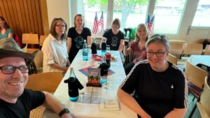 Ein Foto vom Tanztee der Gruppe "Just For Fun", auf dem mehrere Mitglieder der HNT Jolly Boots gemeinsam am Tisch sitzen und in die Kamera lächeln.