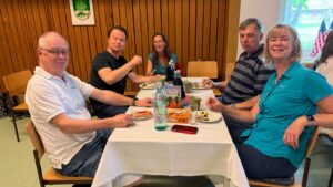 Ein Foto vom Tanztee der Gruppe "Just For Fun", auf dem mehrere Mitglieder der HNT Jolly Boots gemeinsam am Tisch sitzen und in die Kamera lächeln.