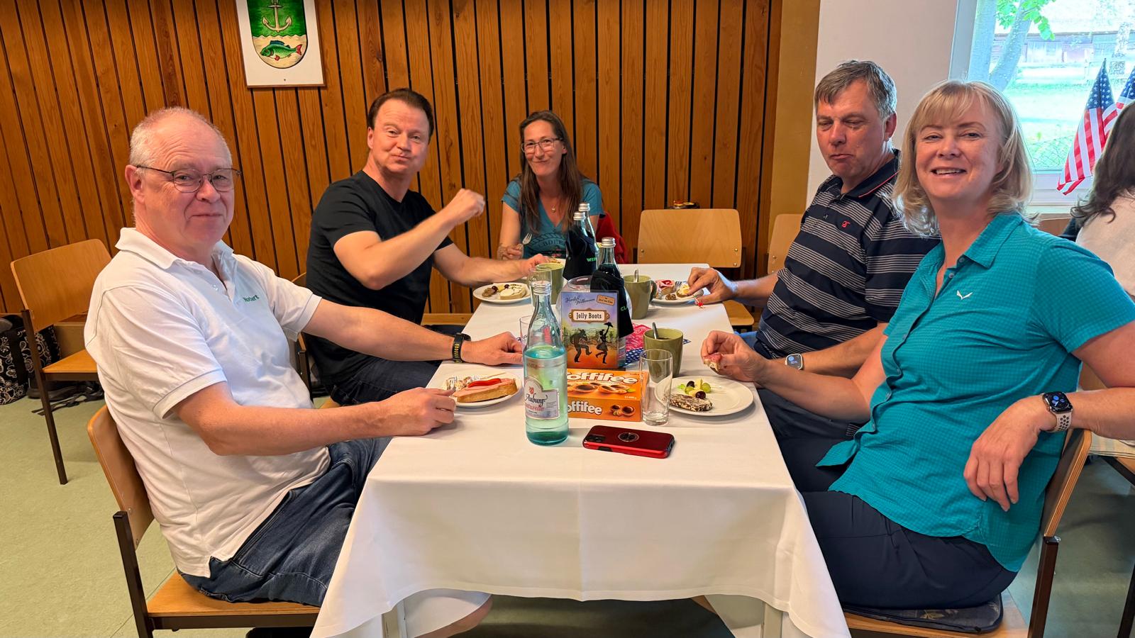 Ein Foto vom Tanztee der Gruppe "Just For Fun", auf dem mehrere Mitglieder der HNT Jolly Boots gemeinsam am Tisch sitzen und in die Kamera lächeln.
