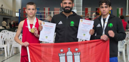 Ein Foto von Andri Manankov und Orlando Christiansen bei der DM, auf dem sie zusammen mit HNT-Trainer Hasan Kiraz eine Fahne der Stadt Hamburg in die Kamera halten.