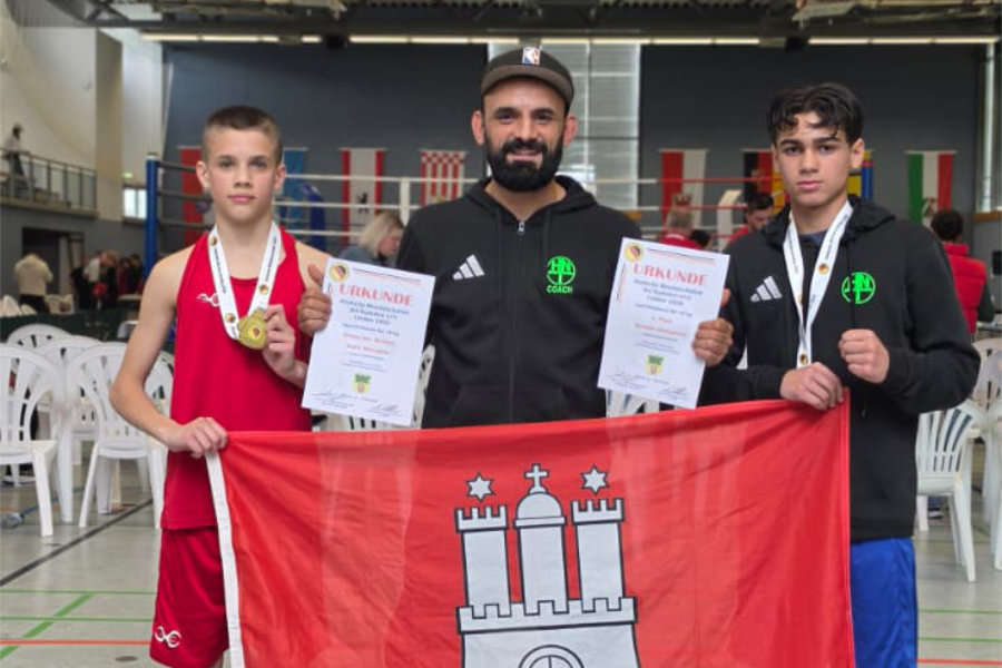 Ein Foto von Andri Manankov und Orlando Christiansen bei der DM, auf dem sie zusammen mit HNT-Trainer Hasan Kiraz eine Fahne der Stadt Hamburg in die Kamera halten.