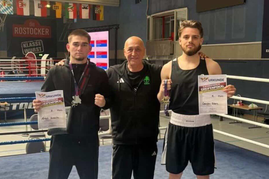 Ein Foto von Carsten Ehlers und Ashab Ismailov beim Greifenpokal, auf dem sie nebeneinander zusammen mit ihrem Trainer im Ring stehen und ihre Urkunden präsentieren.