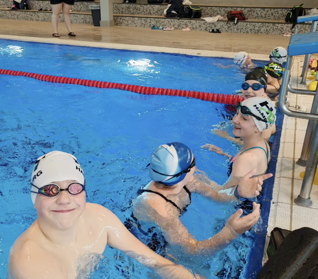 Kurztrainingslager HNT Schwimmen Mai 2026 Ein Foto von mehreren HNT-Schwimmer:innen, die im Schwimmbecken am Rand unterhalb der Startblöcke warten.