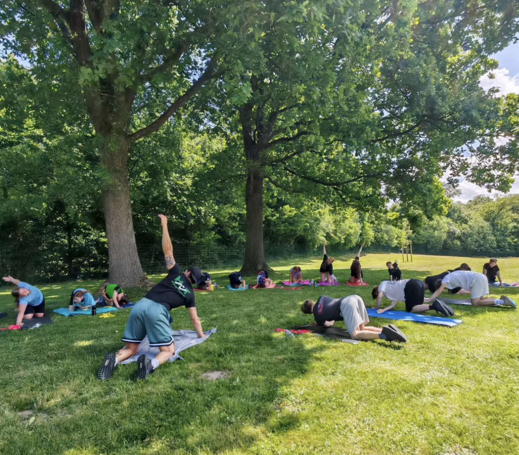 Kurztrainingslager HNT Schwimmen Mai 2026 Ein Foto von der HNT-Trainingsgruppe beim Stretching auf einer Wiese.
