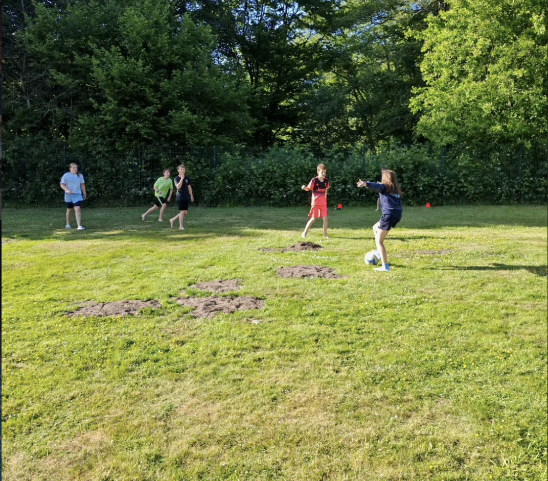 Kurztrainingslager HNT Schwimmen Mai 2026 Ein Foto von mehreren HNT-Schwimmer:innen, die auf einer Wiese Fußball spielen.