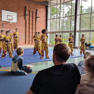 Ein Foto vom HNT Ju-Jutsu-Showteam bei einem Auftritt in der Sporthalle, drumherum sitzen Zuschauer.