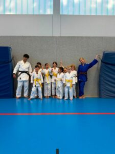 Ein Gruppenfoto in der Sporthalle von den jungen Judoka mit ihren Prüfern Briana und Brian.