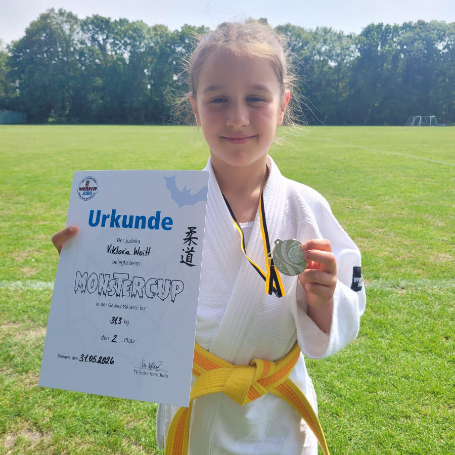 Ein Foto von Viktoria, die draußen auf einer Wiese steht und ihre Urkunde und die Medaille für den zweiten Platz hochhält.
