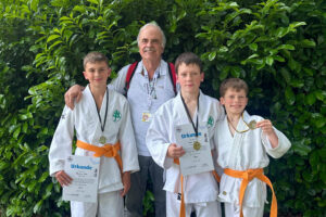 Ein Foto von Trainer Michael Zart zusammen mit Maximilian, Roman und Mark, die alle ihre Urkunden und Medaillen vom Monstercup hochalten.