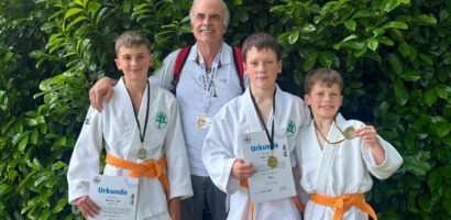 Ein Foto von Trainer Michael Zart zusammen mit Maximilian, Roman und Mark, die alle ihre Urkunden und Medaillen vom Monstercup hochalten.