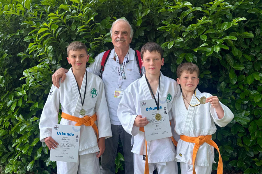 Ein Foto von Trainer Michael Zart zusammen mit Maximilian, Roman und Mark, die alle ihre Urkunden und Medaillen vom Monstercup hochalten.