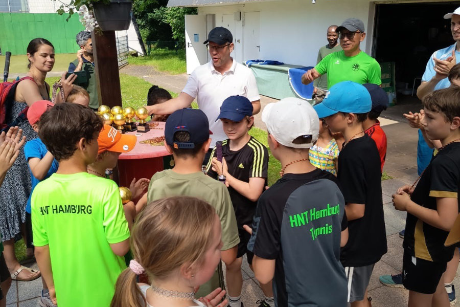 Ein Foto der teilnehmenden Kinder, die sich um einen Stehtisch versammelt haben, auf dem Pokale und Medaillen liegen für die Siegerehrung.