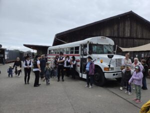 Ein Foto von Mitgliedern der Jolly Boots, die vor einem alten Schulbus stehen, der auf dem Landhof steht.