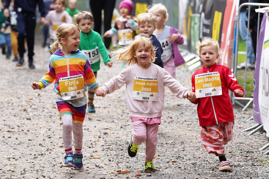 Ein Foto von drei kleinen Kindern, die beim Bambini-Lauf nebeneinander Richtung Ziel laufen und sich dabei an den Händen halten.