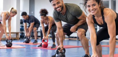 Ein mit KI erstelltes Foto, das mehrere Personen beim Training mit Kugelhanteln in einer Sporthalle zeigt, zwei Personen lächeln dabei freundlich in die Kamera.
