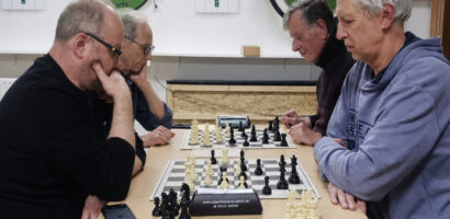 Ein Foto von vier Mitgliedern der Schachabteilung, die rechts und links an einem Tisch sitzen, zwischen ihnen stehen zwei Schachbretter.